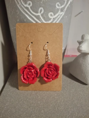 Röda rosformade örhängen - Unika örhängen som är handgjorda i lera, form av röda rosor med krokfäste i silver. Blommorna är detaljerade och har en glansig finish som ger ett snyggt intryck. Perfekta för dig som vill sticka ut med ett romantiskt och kreativt smycke.