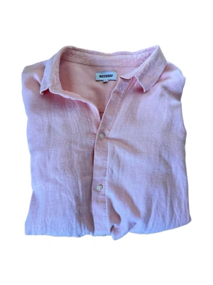 Ljusrosa linneskjorta från Weekday - Säljer en ljusrosa skjorta från Weekday i mjukt linne. Skjortan har klassisk krage, knappar framtill och långa ärmar. Perfekt för en chill och stilren look. Sitter L/XL