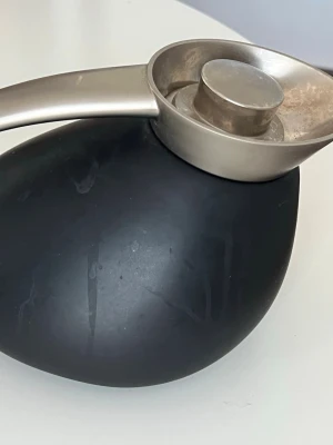 Svart thermos från Georg Jensen - Modern thermos från Georg Jensen i svart sten med ett elegant handtag och skål i borstat rostfritt stål. Stenen har en rundad, organisk form och handtaget ger en cool kontrast mellan material och färg. Perfekt som inredningsdetalj.