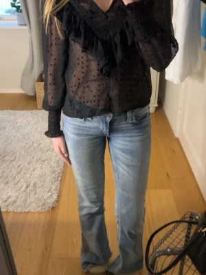 Svart blus från ONLY - Snygg svart blus från ONLY med volangdetaljer och prickigt mönster. Blusen har långa ärmar med smock vid ärmslut och v-ringning. Perfekt att styla med jeans eller kjol för en trendig look.