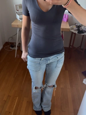 Mörkgrå urringad T-shirt storlek s - Säljer ett par ljusblå jeans med raka ben och stora slitningar vid båda knäna. Jeansen har klassiska fickor fram och bak och en avslappnad passform. Perfekta för en trendig och avslappnad stil.