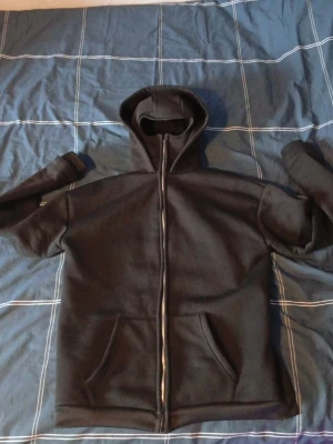 Svart hoodie med dragkedja - Säljer en svart hoodie med dragkedja och som en mask om man drar upp dragkedjan hela vägen sen en luva finns det med. Hoodien har en klassisk huva och är tillverkad i ett mjukt, tjockt material som passar perfekt för chill dagar. Enkel och stilren design utan synligt märke. Bara testad säljer pågrund av att dne är förstör köpt för 600 säljer för 400