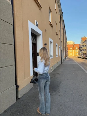 Blå bootcut jeans med slitningar - Säljer ett par snygga blå bootcut jeans med lätt slitning och klassiska bakfickor. Jeansen har en hög midja och är tillverkade i stretchigt denim som sitter skönt. Perfekta för dig som gillar en avslappnad men trendig look.