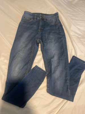 Blå high waist jeans med raka ben - Säljer ett par klassiska blå jeans med hög midja och raka ben. Jeansen har fem fickor, gylf med dragkedja och knapp samt kontrastsömmar. Perfekta för en avslappnad och stilren look. 