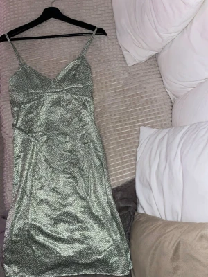 Grön prickig satinklänning - Snygg grön klänning i satin med små vita prickar, helt ny och oanvänd, klänningen är i stl L men passar bättre S-M då den annars blir lite tajt runt magen och höfterna. På sidan finns en dragkedja och banden är justerbara.