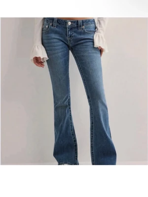 Blå bootcut jeans från True Religion - Säljer ett par blå bootcut jeans från True Religion med klassiska kontrastsömmar och ikoniska fickdetaljer bak. Jeansen har normal midja och är tillverkade i mjuk denim med lätt tvättad look. Perfekta för dig som gillar retrovibbar och snygg passform.