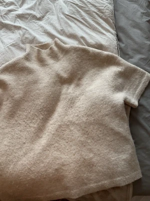 Beige stickad t-shirt med hög krage - Beige stickad tröja med krage. Använd och är nopprig på framsidan. 