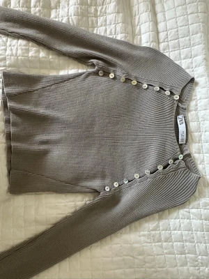 Populär ribbad topp med knappar från Zara - Snygg beige ribbad topp från Zara med lång ärm och dekorativa knappar längs framsidan. Toppen är i storlek S
