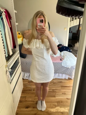 Vit offshoulder kortklänning med volang - Säljer en supersöt student klänning som tyvärr var lite stor för mig. Helt ny med prislapp! Är storlek L men passar en M och nästan en S💕