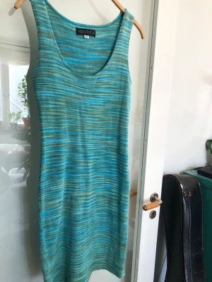 Stickad klänning i tirkosa toner från Ambra Stl S/M - Säljer en stickad klänning från Ambra i blåa och gröna toner med smala ränder. Klänningen är ärmlös, har rund halsringning och är figurnära. 