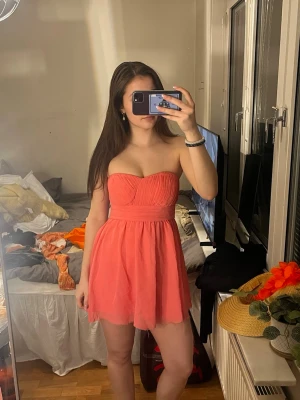 Axelbandslös kort rosa klänning - Söt axelbandslös kort klänning i en härlig rosa nyans. Klänningen har ett markerat midjeband och lätt vippig kjol med draperad överdel. Perfekt för sommarens alla tillfällen och ger en fräsch och ungdomlig look.