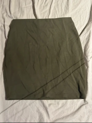 Grön kjol  - Säljer en stilren olivgrön kortkjol i stretchigt material. Tight modell som sitter fint på kroppen och är enkel att matcha till både vardag och fest. Superfin med crop top, stickad tröja eller oversized t-shirt för en avslappnad men snygg look.(ifrån new yorker) 