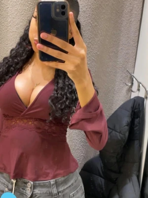 Vinröd omlottopp med spetsdetalj - Vinröd topp med v-ringning och spetsdetalj. Toppen har långa ärmar och lätt utsvängd nederdel. Kontakta vi med frågor💕