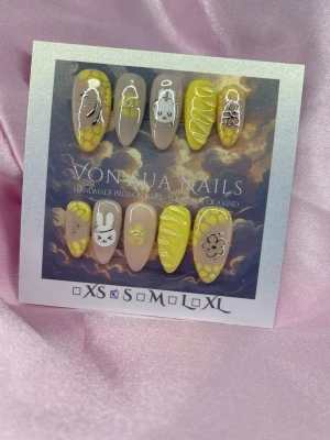 MiffyLemon (S);Medium Almond - Unika handgjorda press-on naglar i en medium lång mandelform. Setet har en mix av nude beige och gula naglar med söta motiv som kaniner(Miffy), blommor och grafiska detaljer. S: 15 mm, 11,5 mm, 12 mm, 11 mm, 9 mm, och designen är lekfull och trendig – perfekt för dig som vill sticka ut.