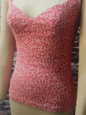 Blommig rosa linnetopp - Söt rosa linnetopp med småblommigt mönster. Toppen är ärmlös med smala axelband och har en figurnära passform. Perfekt för varma dagar och enkel att matcha med jeans eller kjol.