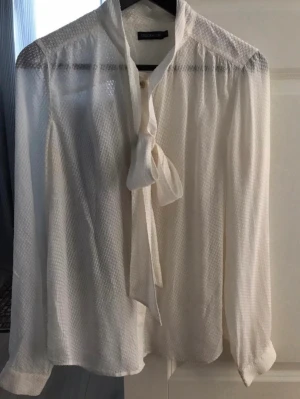 Vit blus med knyt från STOCKH LM - Snygg vit blus från STOCKH LM i storlek 38. Blusen har långärmad design, knytband i halsen och ett diskret rutmönster i tyget. Tillverkad i ett lätt och luftigt material som ger en elegant look. Perfekt att styla med jeans eller kjol. Kolla gärna mina andra annonser❗️