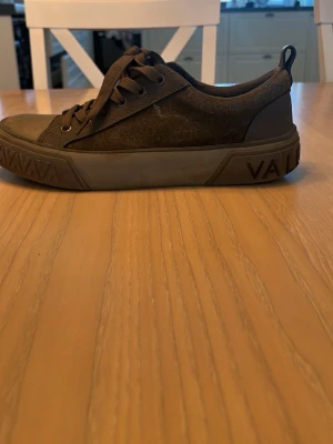 Mörkgrå sneakers från Valentino - Snygga mörkgrå sneakers från Valentino med klassisk låg profil. Skorna har en robust gummisula med tydligt mönster och ovandel i textil och syntet. Matchande grå skosnören och diskret logga på innersulan. Perfekta för en stilren och avslappnad look. 