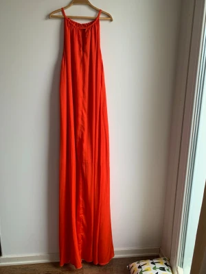 STOCKH LM orange ärmlös klänning stl M - Lång klänning i en livlig orange nyans med smala axelband och en smickrande passform. Klänningen har en elegant design som passar för många tillfällen. Den är helfodrad och har en diskret knäppning i nacken.