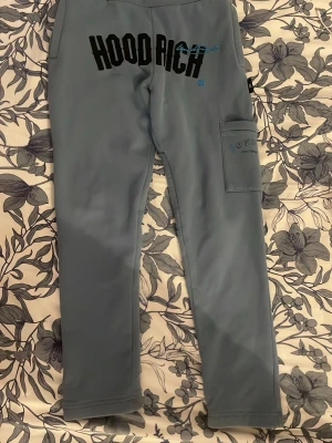 Blå hoodrich byxor S - Säljer ett par blå leggings med smal passform och en praktisk ficka på ena benet. Perfekta för en avslappnad stil och lätta att matcha med olika toppar. Materialet känns mjukt och stretchigt för extra komfort.