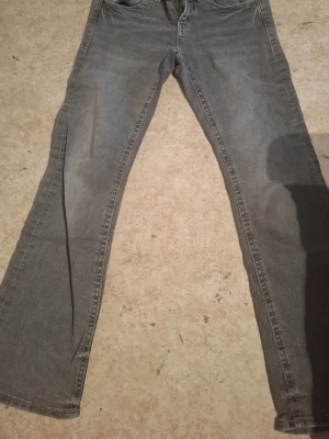 Grå bootcut jeans med fickor bak - Säljer ett par grå bootcut jeans med klassisk femficksdesign och snygga detaljer på bakfickorna. Jeansen har lågl midja. Perfekta för dig som gillar en retrostil.
