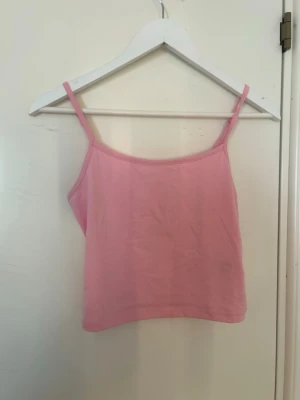 Ljusrosa linnetopp med smala band - Söt ljusrosa linnetopp med smala axelband och rak passform. Toppen är ärmlös och croppad, perfekt för varma dagar. Enkel och stilren design som är lätt att matcha med olika outfits.