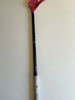Innebandyklubba med rosa blad - Säljer en innebandyklubba från Oxdog med svart skaft och ett rosa blad. Skaftet har vita detaljer och greppet är lindat med ljus går oj. Perfekt för dig som gillar innebandy och vill sticka ut på planen. Balder och klubban är helt nya, använt 1 gång kanske.
