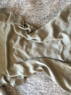 Ljusgrön blus med volang från Zara - Snygg ljusgrön blus från Zara Basic i ett tunt, flowy material. Blusen har volangdetaljer vid halsen och ärmarna, vilket ger en romantisk vibe. Perfekt att styla med jeans eller kjol för en trendig look.