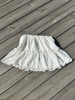 Vit volangkjol  - Supersöt vit kortkjol med volanger och diskret prickigt mönster. Kjolen har resår i midjan och är gjord i ett lätt, luftigt tyg. Det står ingen stolek men skulle säga att den är mellan S-M