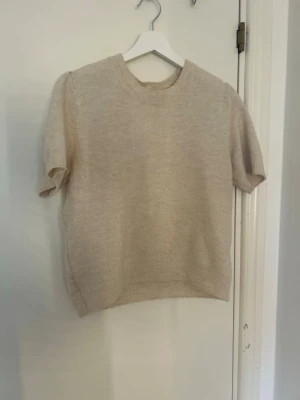Beige stickad kortärmad tröja H&M - Stickad kortärmad tröja från H&M i mjuk beige ton. Tröjan har rund halsringning och ribbade kanter vid ärmslut och nederkant. Perfekt för lager på lager och enkel att matcha med olika stilar.