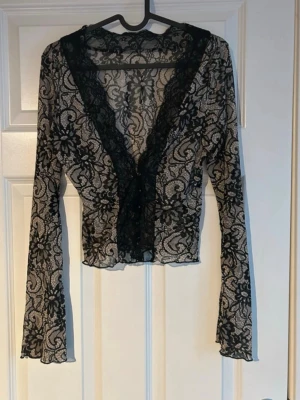 Spets topp  - Transparent svart spetstopp med djup V-ringning och dekorativa knappar framtill med långa ärmar och detaljerat blommigt spetsmönster  Perfekt för dig som gillar en lite mer vågad och trendig stil. Supersnygg till höga jeans eller kjol!(ifrån shein) 