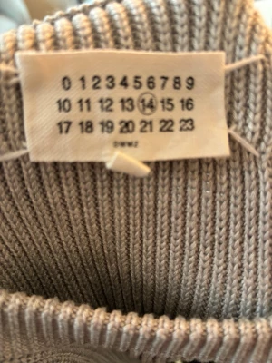 Beige stickad tröja från Maison Margiela - Säljer en beige stickad tröja från Maison Margiela. Tröjan har en ribbstickad struktur, rund halsringning och långa ärmar. Perfekt för dig som gillar minimalistisk och stilren design.