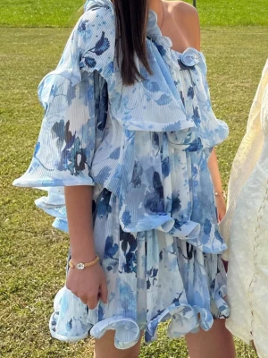 Blåvit oneshoulder volangklänning - Supersöt kort klänning i blått och vitt med blommigt mönster. Klänningen har oneshoulder-design med volanger. Den är ifrån NA-KD och är helt slutsåld. Köpte den på Plick, men ändrade mig att jag ville ha en annan klänning. Går troligtvis ner i pris vid snabb affär, andvänd gärna ”köp nu”