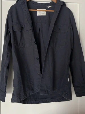 Marinblå overshirt från Jack&Jones - Mörkblå overshirt från Jack&Jones. Skjortan har två bröstfickor med knappar, långa ärmar och knäppning framtill. Tillverkad i mjuk bomull och har en avslappnad passform. Perfekt för en chill och stilren look.