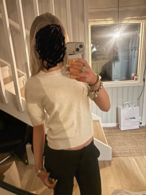 Vit stickad t-shirt med kort ärm - Säljer en vit stickad t-shirt med korta ärmar och rund hals. Tröjan har ribbade detaljer vid halsringning, ärmslut och nederkant. Perfekt för dig som gillar en enkel men stilren look. 