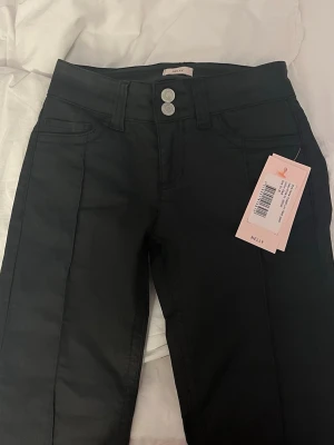 Svarta coated low waist jeans Nelly - Snygga svarta coated low waist jeans från Nelly med dubbla silverknappar i midjan och klassisk femficksdesign. Säljer då de tyvärr var för små för mig, prislapp sitter kvar, endast testade💞