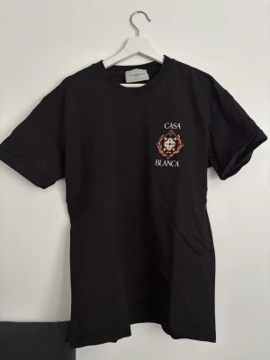 Svart Casa Blanca t-shirt med tryck - Snygg svart t-shirt från Casablanca med färgglatt tryck och texten 'Casa Blanca' både fram och bak. Klassisk passform med korta ärmar och rund hals. Tillverkad i mjuk bomull som känns skön mot huden. Perfekt för dig som vill ha en stilren men ändå unik look.