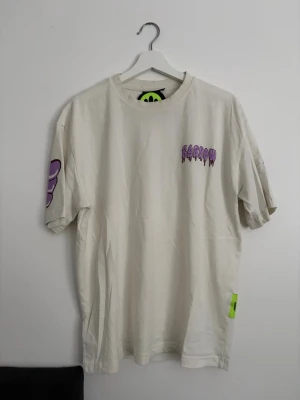 Vit t-shirt med tryck från Barrow - Unik vit t-shirt från Barrow med lila tryck på bröstet och ärmarna samt en stor nallebjörn och text på ryggen. Oversized passform och coola grafiska detaljer gör den till ett statement-plagg. Tillverkad i mjuk bomull för skön känsla.