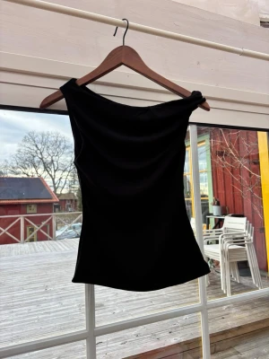 Svart oneshoulder topp - Snygg svart oneshoulder topp med stilren och enkel design. Toppen har en asymmetrisk axel och är figurnära, vilket ger en trendig och modern look. Perfekt att matcha med jeans eller kjol för en cool outfit.