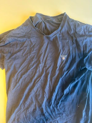 Marinblå t-shirt från GANT - Snygg marinblå t-shirt från GANT med klassisk rund hals och liten broderad logga på bröstet. Tillverkad i mjuk bomull och har en normal passform. Perfekt för en avslappnad och stilren look.