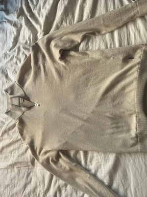 Beige halvzip-tröja från Jack and Jones  - Snygg beige stickad tröja från Jack and Jones  med halvzip och ståkrage. Tröjan har långa ärmar och ribbade muddar vid ärmslut och nederkant. Perfekt för lager på lager och enkel att matcha med olika outfits.