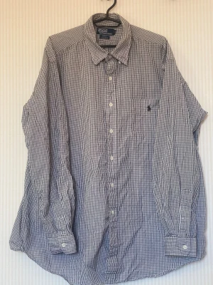 Rutig skjorta från Polo Ralph Lauren - Klassisk rutig skjorta från Polo Ralph Lauren i blått och vitt. Skjortan har lång ärm, knappar framtill och en bröstficka med broderad logga. Tillverkad i mjuk bomull och har en tidlös, normal passform.