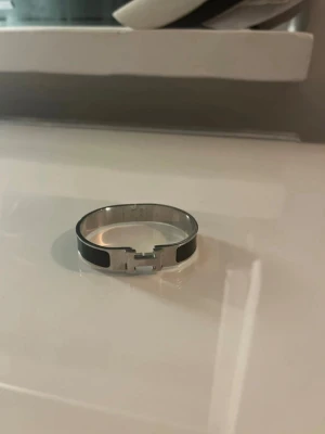 Zara armband svart o vit (H) - Snyggt armband från Zara i silverfärgad metall med svarta detaljer. Armbandet har den ikoniska H-formade låset och en stilren, modern design. Perfekt accessoar för att lyfta din outfit med en exklusiv touch. SJÄLVKLART REP