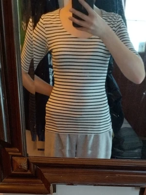 Randig t-shirt från Lindex - Säljer en klassisk vit t-shirt med svarta horisontella ränder från Lindex. T-shirten har rund halsringning och korta ärmar. Tillverkad i mjuk bomull som känns skön mot huden. Perfekt för en enkel och stilren look.