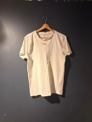 Vit t-shirt från 457 med tryck - Vit t-shirt från 457 med litet rött tryck på bröstet där det står 'PASSION IS A FORM'. Klassisk rak passform och rund halsringning. Tillverkad i mjukt bomullstyg som känns skönt mot huden. Perfekt basplagg för en clean och enkel stil.