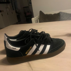 Svarta Adidas Spezial - Säljer ett par Adidas Spezial sneakers i svart mocka med vita detaljer och klassiska tre ränder på sidan och texten YNWA. Skorna är ungefär andvända 2-3 gånger då dom inte passa min storlek.