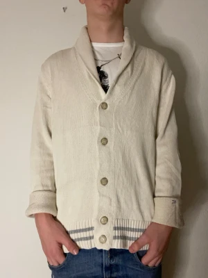 Beige kofta med sjalkrage och knappar - Stilren beige kofta med sjalkrage och stora knappar framtill. Visas på sista bilden hur det ser ut utan uppvikta ärmar. Modellen på bilderna är 178 och väger cirka 70kg. Hör gärna av er vid funderingar eller frågor!