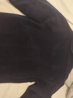 Mörkblå manchester overshirt - Stilren mörkblå overshirt i manchestertyg med klassisk krage och knappstängning framtill. Overshirten har en bröstficka och långa ärmar. Perfekt att bära som lager över en t-shirt för en avslappnad look.