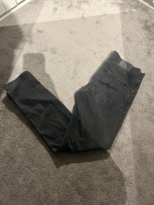 Svarta slim fit jeans från Nudie Jeans - Säljer ett par svarta slim fit jeans från Nudie Jeans med klassisk femficksmodell och diskret logga på bakfickan. Jeansen har en snygg tvättad look och raka ben. Perfekta för dig som gillar stilrena och bekväma jeans. De är i modellen Lean Dean