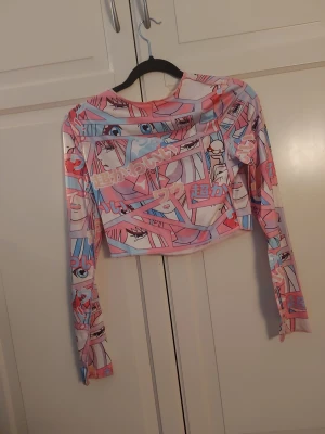 Animeinspirerad croppad långärmad topp - Säljer en färgglad croppad långärmad topp med animeinspirerat tryck i rosa, blått och vitt. Toppen har en slim passform och är perfekt för dig som gillar unik och lekfull stil. Materialet känns stretchigt och lätt.