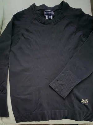 Svart långärmad tröja B Vertigo - Svart/nattblå långärmad teknisk tröja från B Vertigo med rund hals och ribbade muddar vid ärmslut och nederkant.Enkel och stilren design som funkar till träning.Innehåller elastan. Tjockare än helt tunn trikå, som ett mellanskikt på vintern, och som sådan när varmare. Har tumhål på ärmarna. Framdelens mått:  armhåla till armhåla: 47 cm utan att töja (töjer lätt till 50 cm) Längd axel till nedre kant: 61 cm